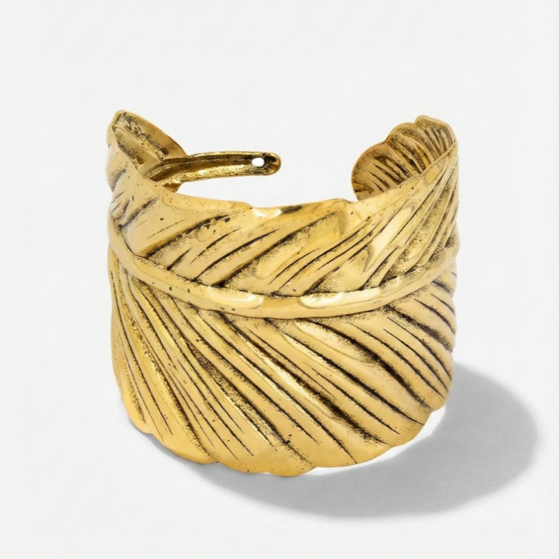 Damenarmreif mit breiter, strukturierter Metalloberfläche und offener Form, in Gold- oder Silberoptik am Handgelenk und in Detailansicht dargestellt